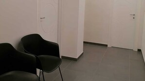 Ein Flur mit zwei schwarzen Stühlen, weißen Türen und eingelassener Deckenbeleuchtung.