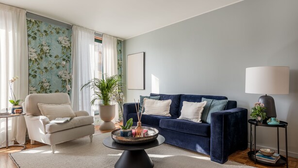 A living room with a dark blue sofa, a white armchair, a black coffee table, and a potted plant. - Charming Duplex in Foz do Douro | Near Passeio Alegre & the Sea (Porto)