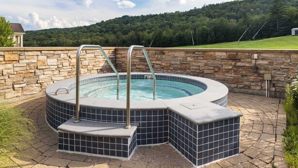 A hot tub with two steps and metal railings, surrounded by stone walls and a stone pathway. - Charming 2-Bedroom Ski-In/Ski-Out at Jackson Gore (Ludlow)