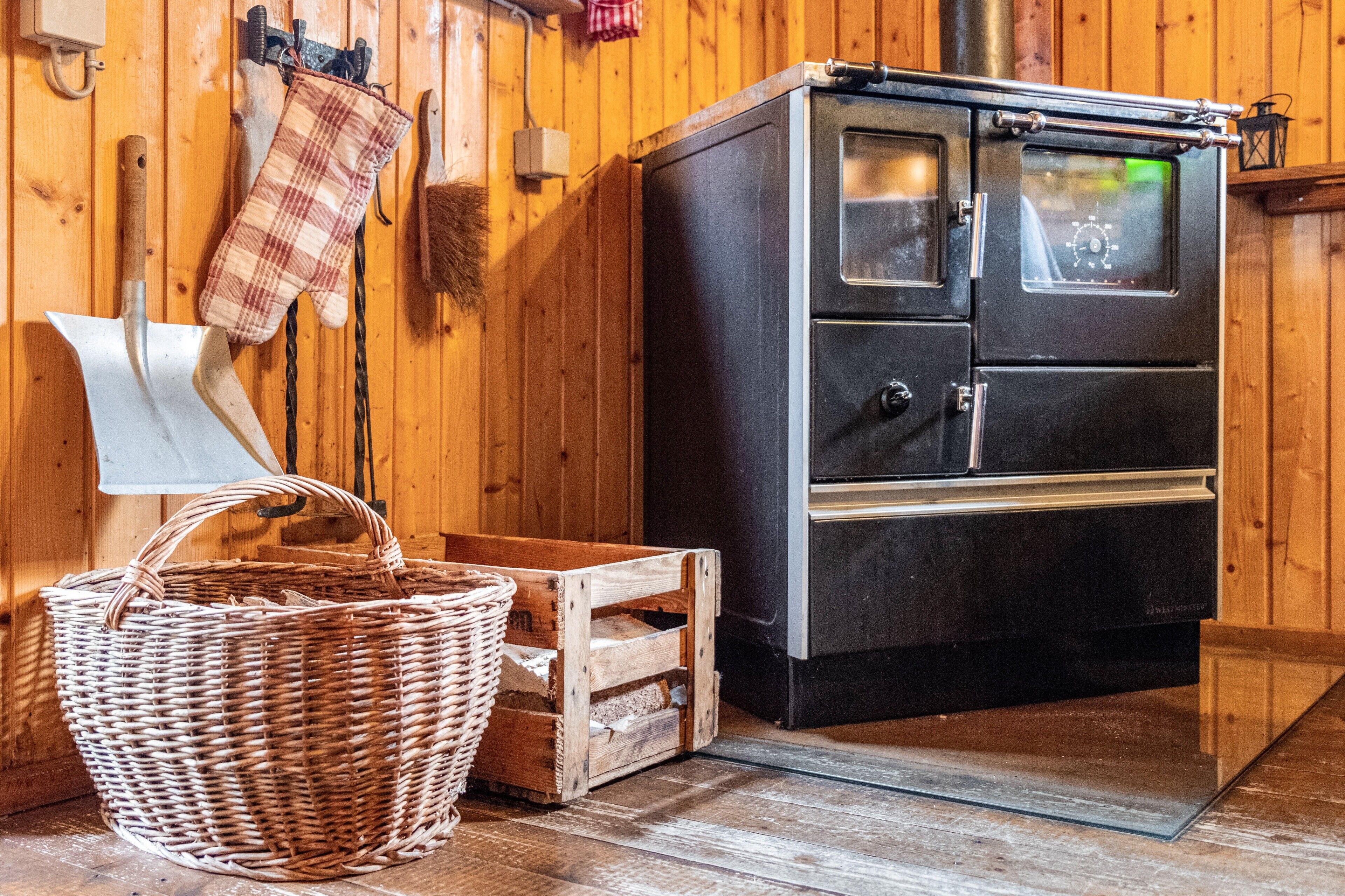 A wooden interior with a black stove, a wicker basket, and a wooden crate.