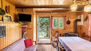 Interior de una cabaña de madera con sofá, mesa, televisor y ventana con cortinas.