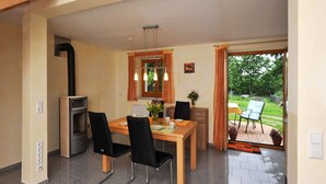 Un espace repas comprenant une table, des chaises, un poêle et donnant sur l’extérieur.