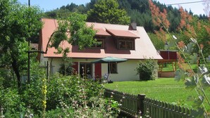 Une maison à deux étages, avec un toit recouvert de tuiles rouges, un porche à l’avant et un parasol vert.