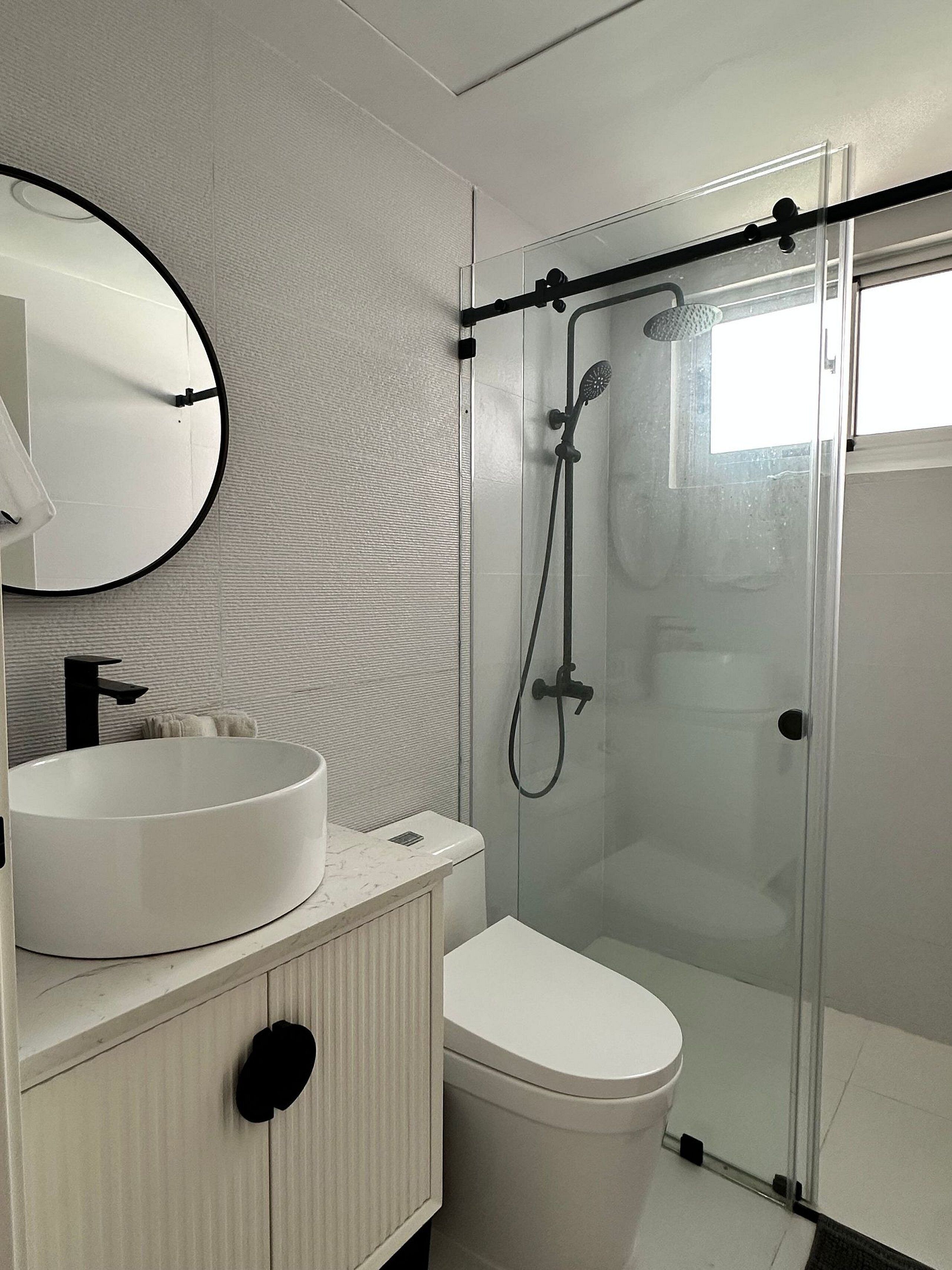 Une salle de bain moderne avec un lavabo rond, des toilettes et une douche à parois de verre.