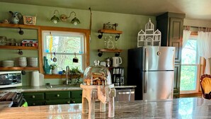 A kitchen with a marble countertop, wicker chairs, a refrigerator, and various kitchen items.