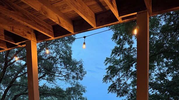 A deck with a square fire pit and string lights.