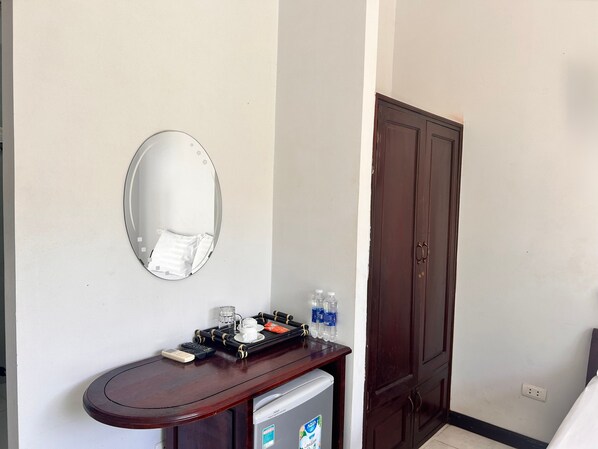Habitación de hotel con tocador de madera, espejo, refrigerador pequeño y puerta de madera.