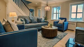 A modern living room with a blue sofa set, a round coffee table, and a staircase with blue railings.