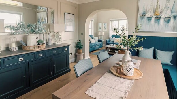 A modern kitchen with dark blue cabinets, a wooden dining table, and a blue sofa in the living area.