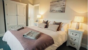 A bedroom with a large bed, two bedside tables, a wardrobe, and a painting on the wall.