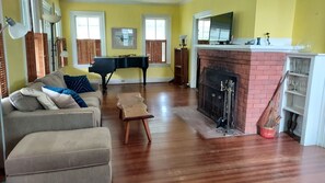 A living room with a sofa, a coffee table, a fireplace, a piano, and a TV.