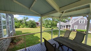 A covered patio with a table and chairs, overlooking a grassy yard and a house.