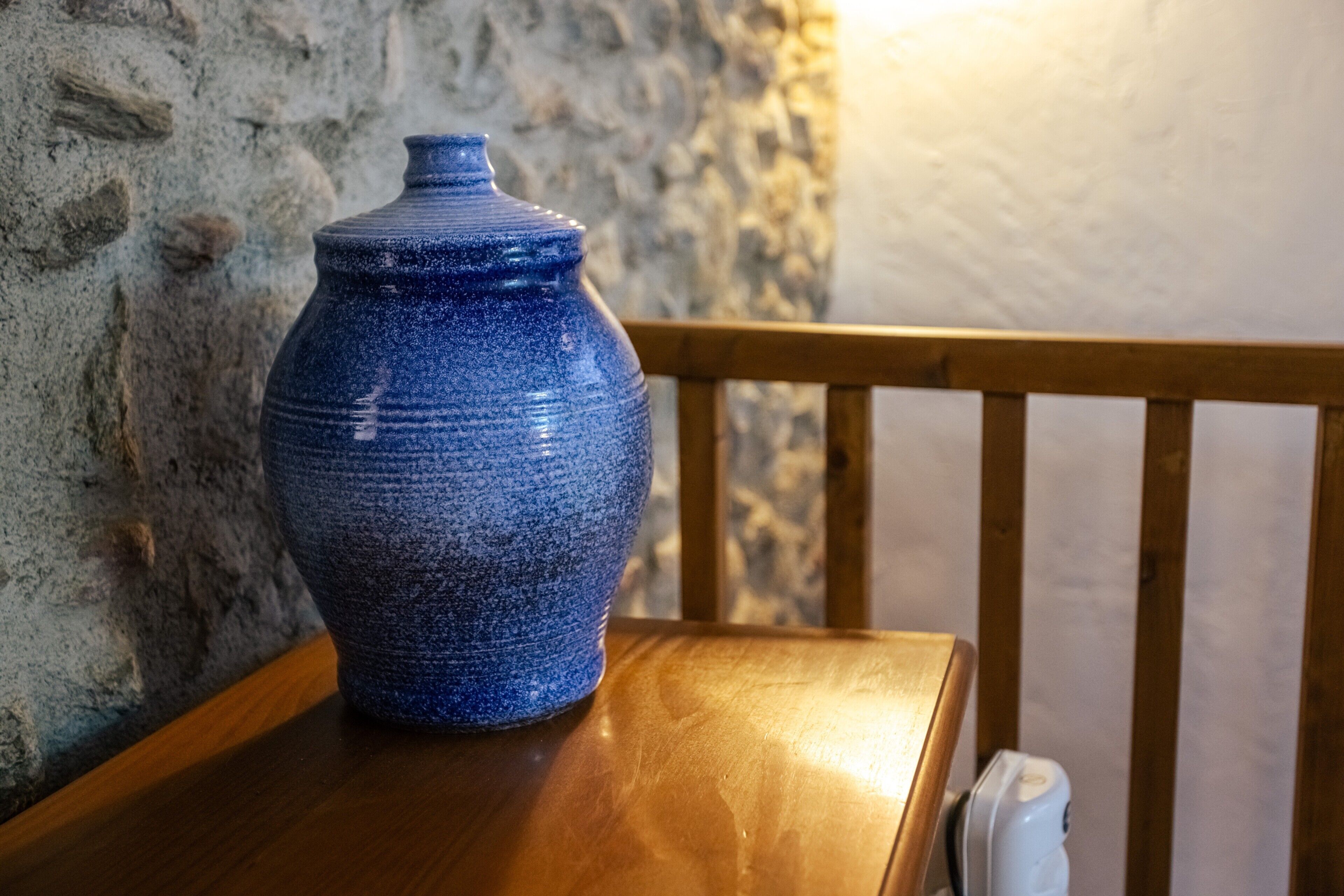 Un jarrón azul de cerámica sobre una mesa de madera frente a una pared de piedra.