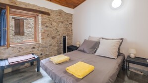 Une chambre avec un mur en pierre, un plafond en bois, un lit avec des oreillers, une table de chevet avec une lampe et un banc.