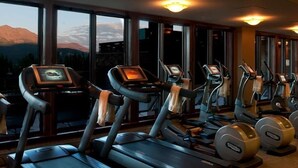 Un gimnasio con cintas de correr y elípticas, amplias ventanas con vista a la montaña e iluminación en el techo.