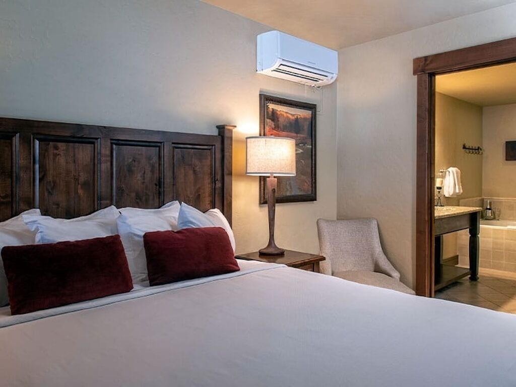 Ein Hotelzimmer mit einem großen Bett, einer Nachttischlampe, einem Sessel, einem Holz-Kopfteil, einem Bild an der Wand und einer Klimaanlage.