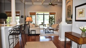 A spacious living area with a sofa, coffee table, and a dining area with a bar. - Live Oaks Cottage - Golf Course Views & Lowcountry Charm in Bluffton, SC (Bluffton)