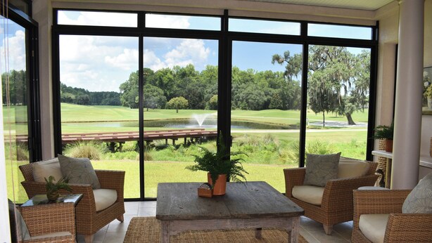 A room with wicker furniture, a view of a golf course, and a large window. - Live Oaks Cottage - Golf Course Views & Lowcountry Charm in Bluffton, SC (Bluffton)