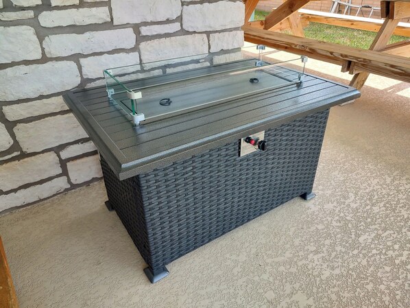 A black outdoor grill with a glass top and metal handles, set against a stone wall.