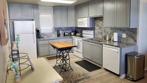 Een moderne keuken met grijze kastjes, een houten tafel en een vaatwasser van roestvrij staal.