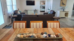Een woonkamer met een bank, stoelen, een televisie, een plafondventilator en een eettafel met decoratieve objecten.