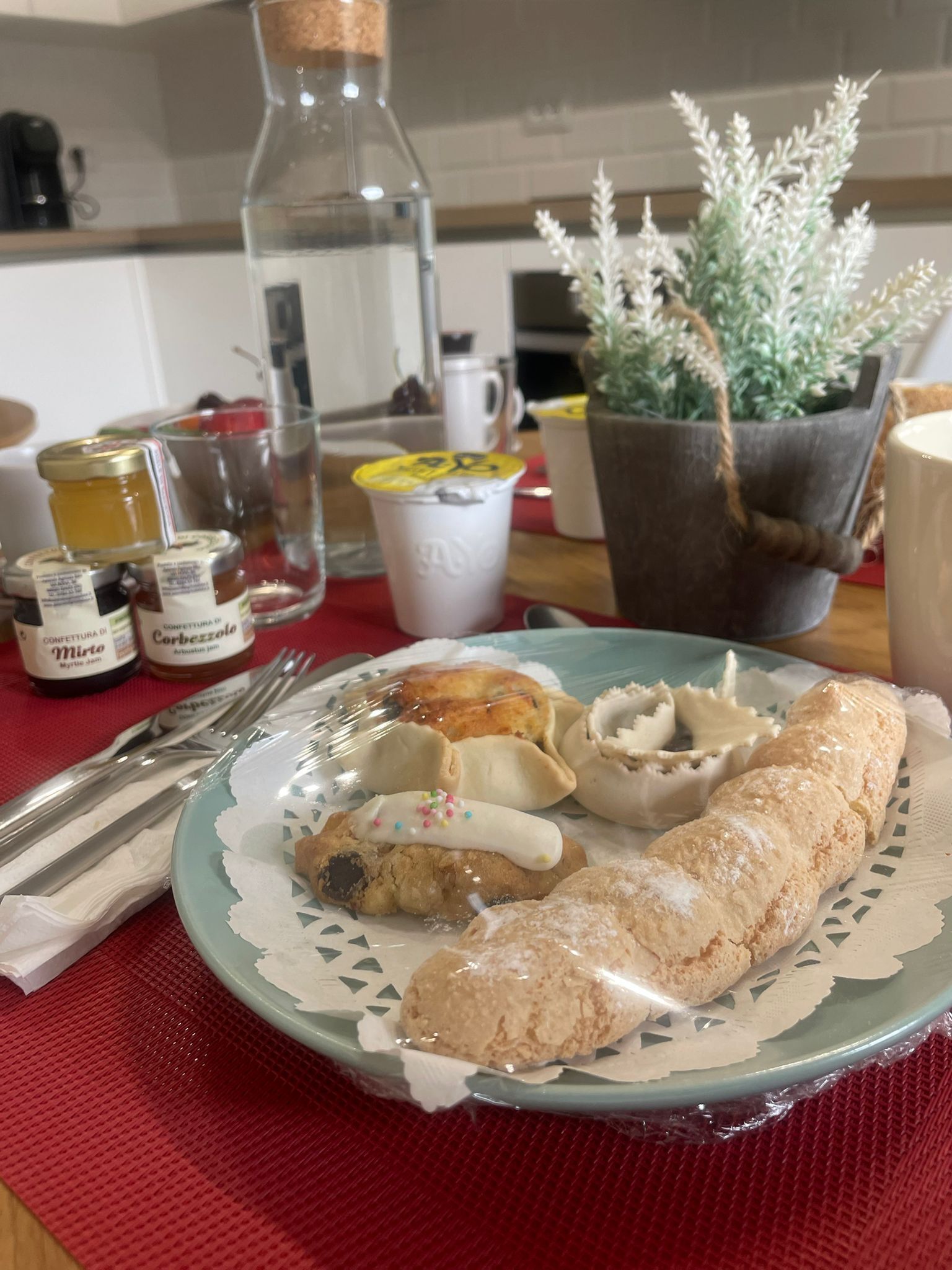 A table with a plate of pastries, a bottle, and jars of jam.