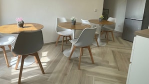 Een moderne keuken met een inbouwkoelkast, houten vloer en een eethoek met ronde tafels en stoelen.