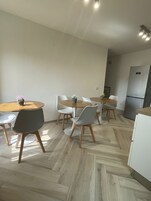 Una cocina moderna con refrigerador empotrado, piso de madera y un comedor con mesas y sillas redondas.