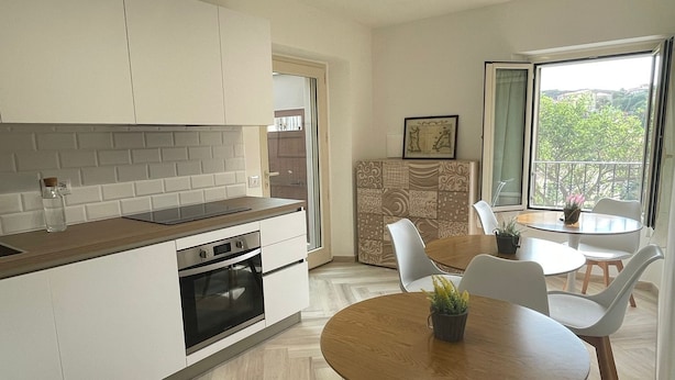 Een moderne keuken met witte kastjes, een houten aanrecht en een inbouwoven. Er is een eethoek met een ronde houten tafel en witte stoelen.