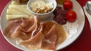 Een bord met diverse soorten eten, zoals brood, kaas, ham en tomaten.