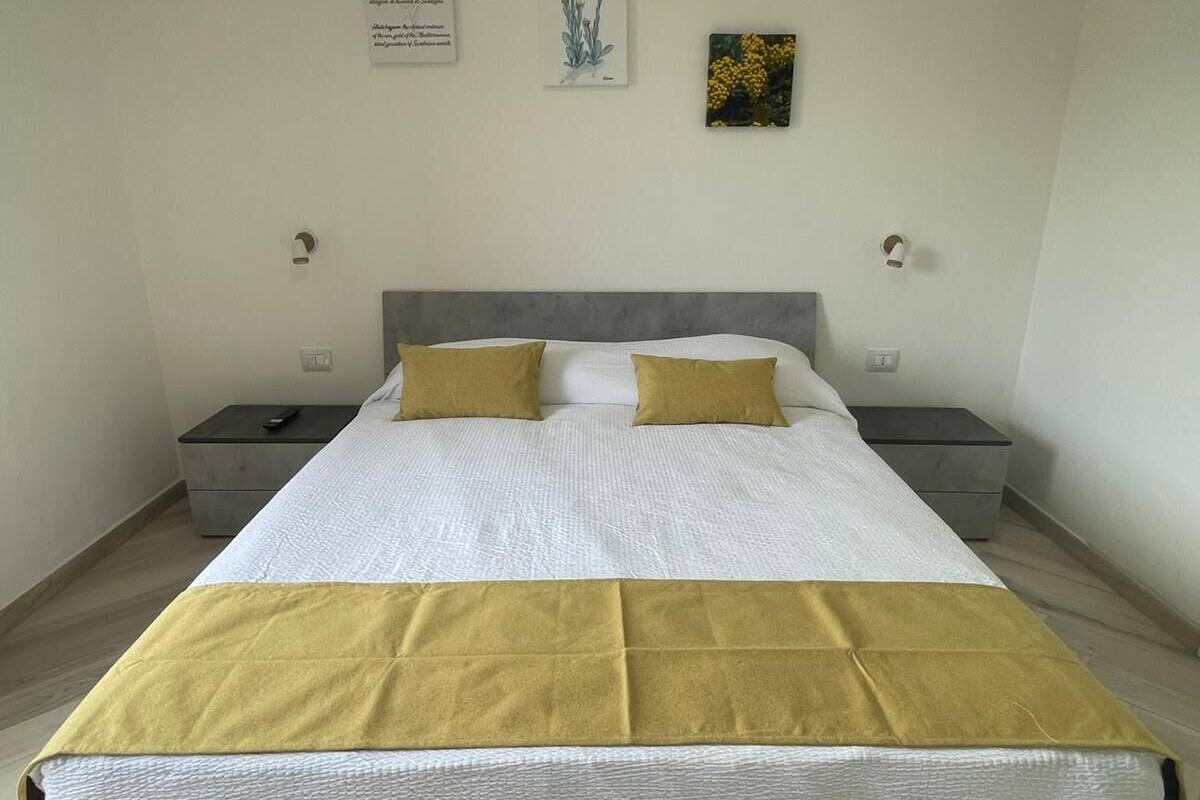 A neatly made bed with a white and yellow bedspread, two bedside tables with lamps, and a wall with two framed pictures.