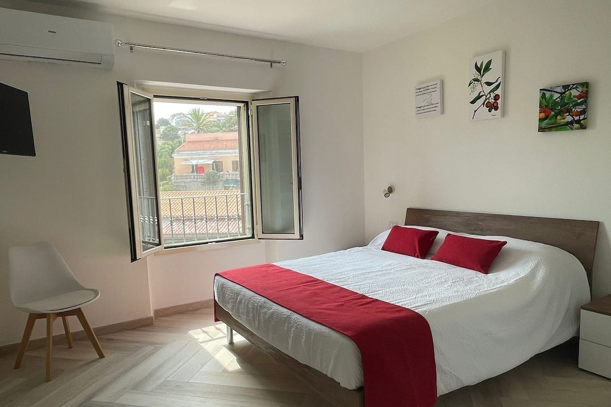 A bedroom with a bed, a chair, a window, and artwork on the wall.