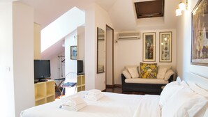 Un dormitorio con cama, sofá, televisión y obras de arte en las paredes.