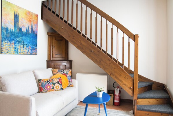 A staircase with wooden railings, a white sofa with colorful pillows, a small blue table with a plant, and a painting on the wall. - La Milanesina - One Bedroom Apartment, Sleeps 4 (Milan)