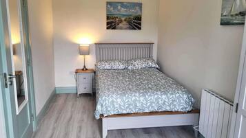 Un dormitorio con una cama, una mesita de noche con lámpara, un cuadro en la pared y una puerta.