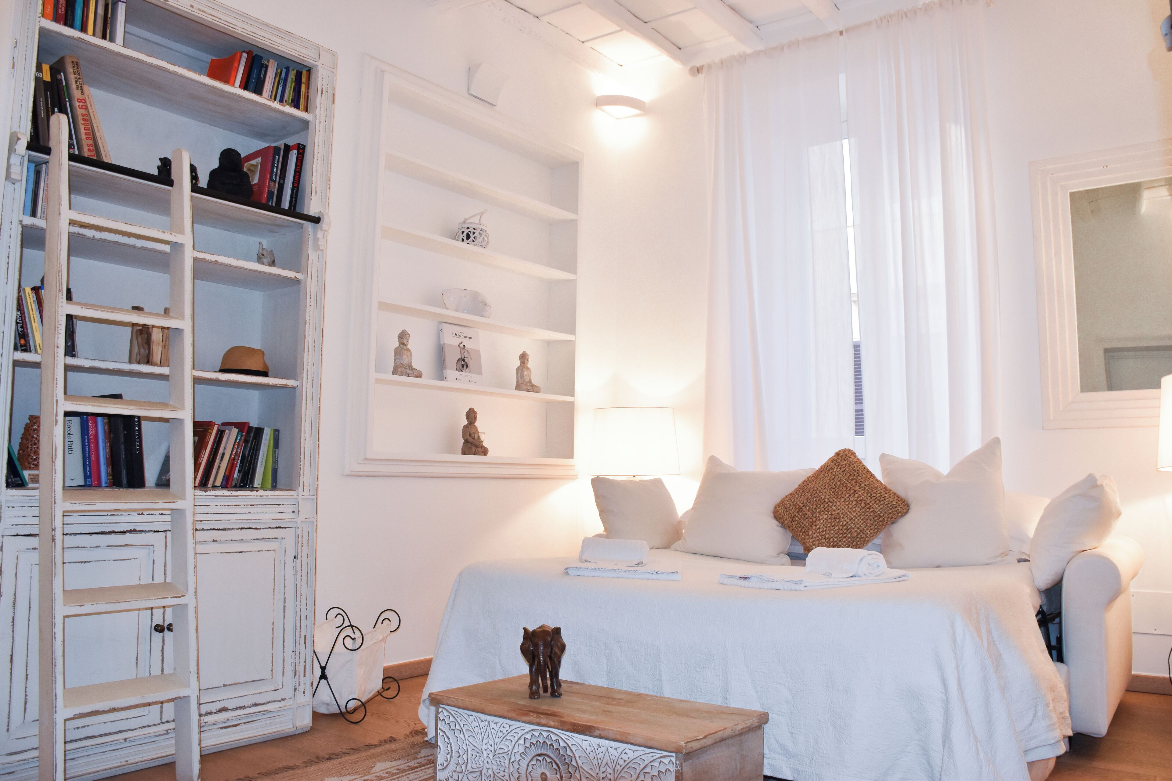Een slaapkamer met een bed, nachtkastjes, een lessenaar, een boekenplank en een raam met gordijnen.