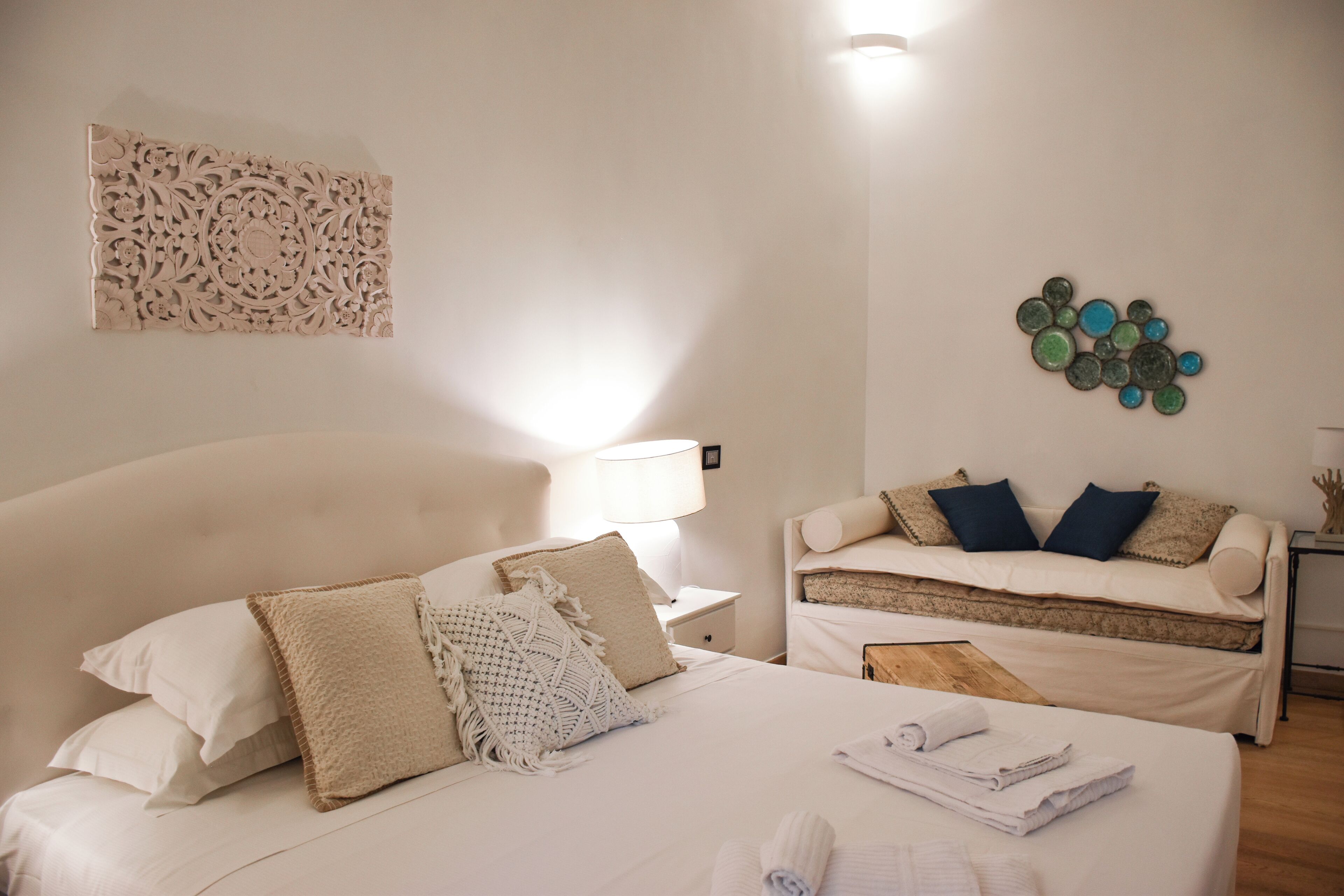 Habitación de hotel con una cama grande, un sofá más pequeño, un adorno de pared y una mesita de noche con lámpara.