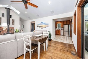 A modern kitchen with wooden cabinets, a stainless steel refrigerator, and a dining area with a wooden table and white chairs.