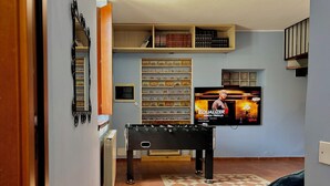 Ein gemütliches Wohnzimmer mit einem Kicker, einem Fernseher, der einen Filmplakat zeigt, und Regalen mit Büchern und Dekoration.