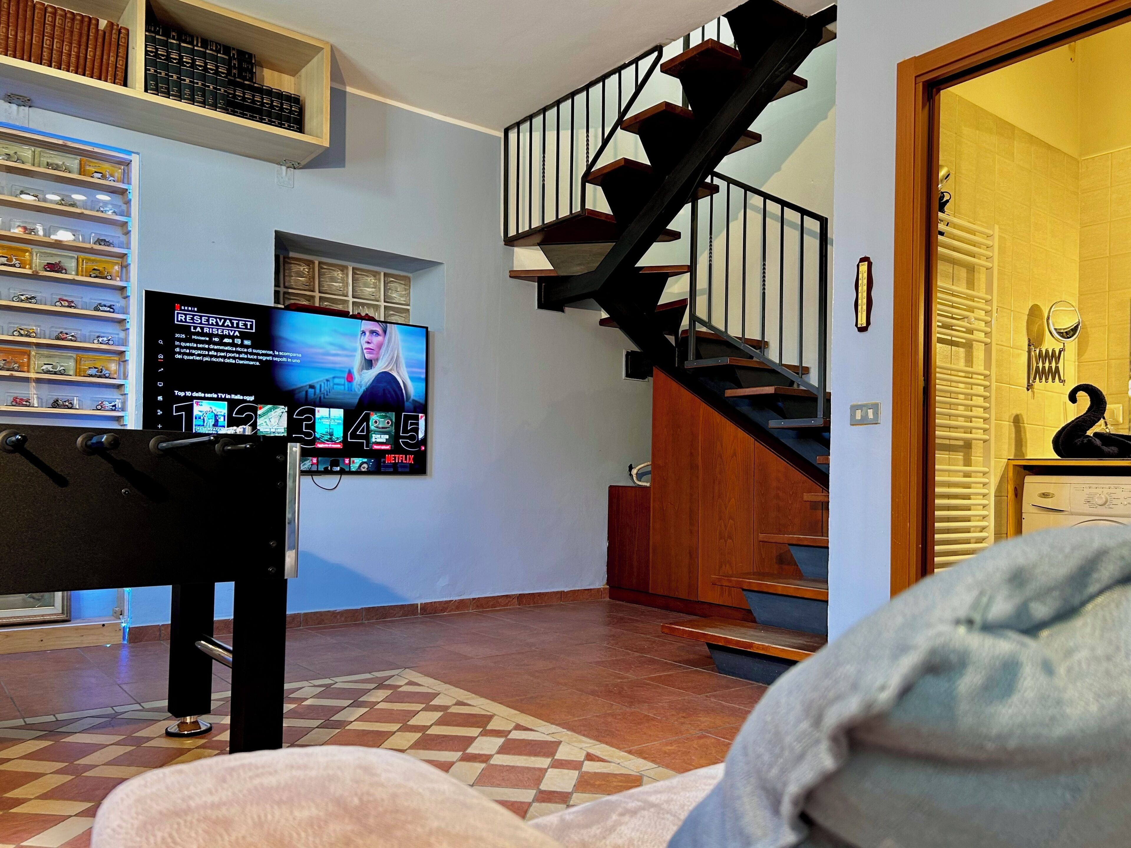 A living room with a TV displaying a streaming service interface, a staircase, and a door leading to another room.