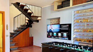 Ein Zimmer mit einer Holztreppe, einem Tischkicker und einem an der Wand befestigten Fernseher, der einen Filmplakat zeigt.