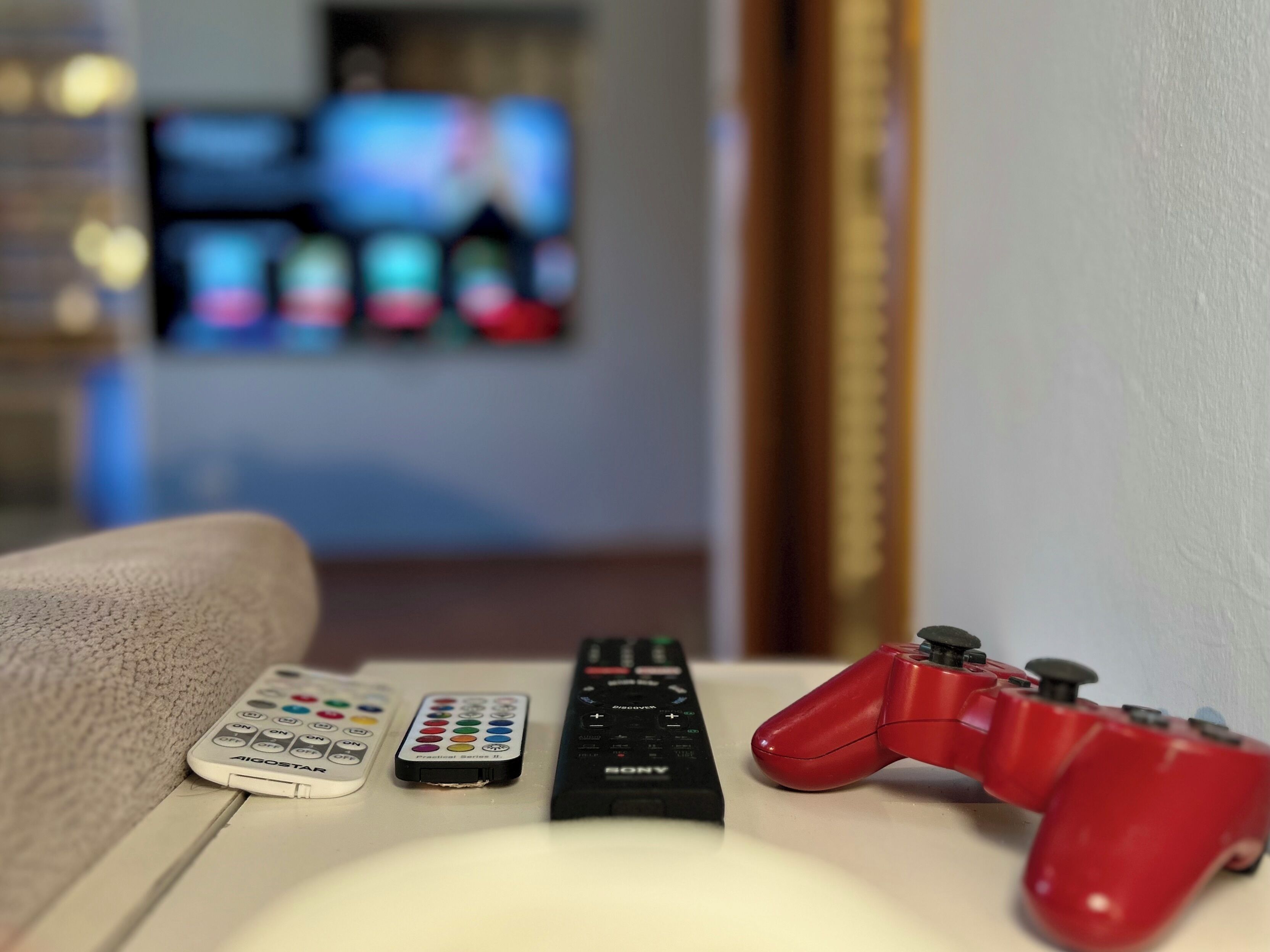 A remote control, a game controller, and a TV remote on a table.