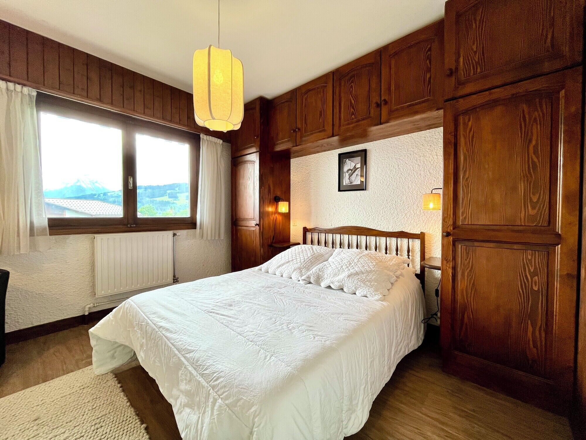 Ein Schlafzimmer mit einem großen Bett, Holzvertäfelung, einem Fenster mit Ausblick und einer Wandleuchte.
