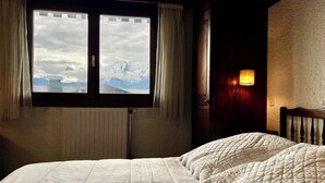 A bedroom with a large window, a radiator, and a bedside lamp. - 80 m² apartment with terrace (Combloux)