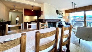 A dining area with wooden chairs and a table, a kitchen with red cabinets, and a fireplace. - 80 m² apartment with terrace (Combloux)