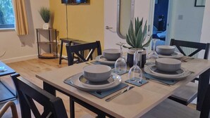 Un coin repas avec une table dressée pour quatre personnes, des chaises, un téléviseur fixé au mur et une porte donnant sur une autre pièce.