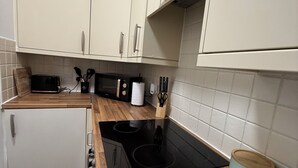 Une cuisine de taille réduite avec des meubles blancs, une cuisinière noire et des plans de travail en bois.