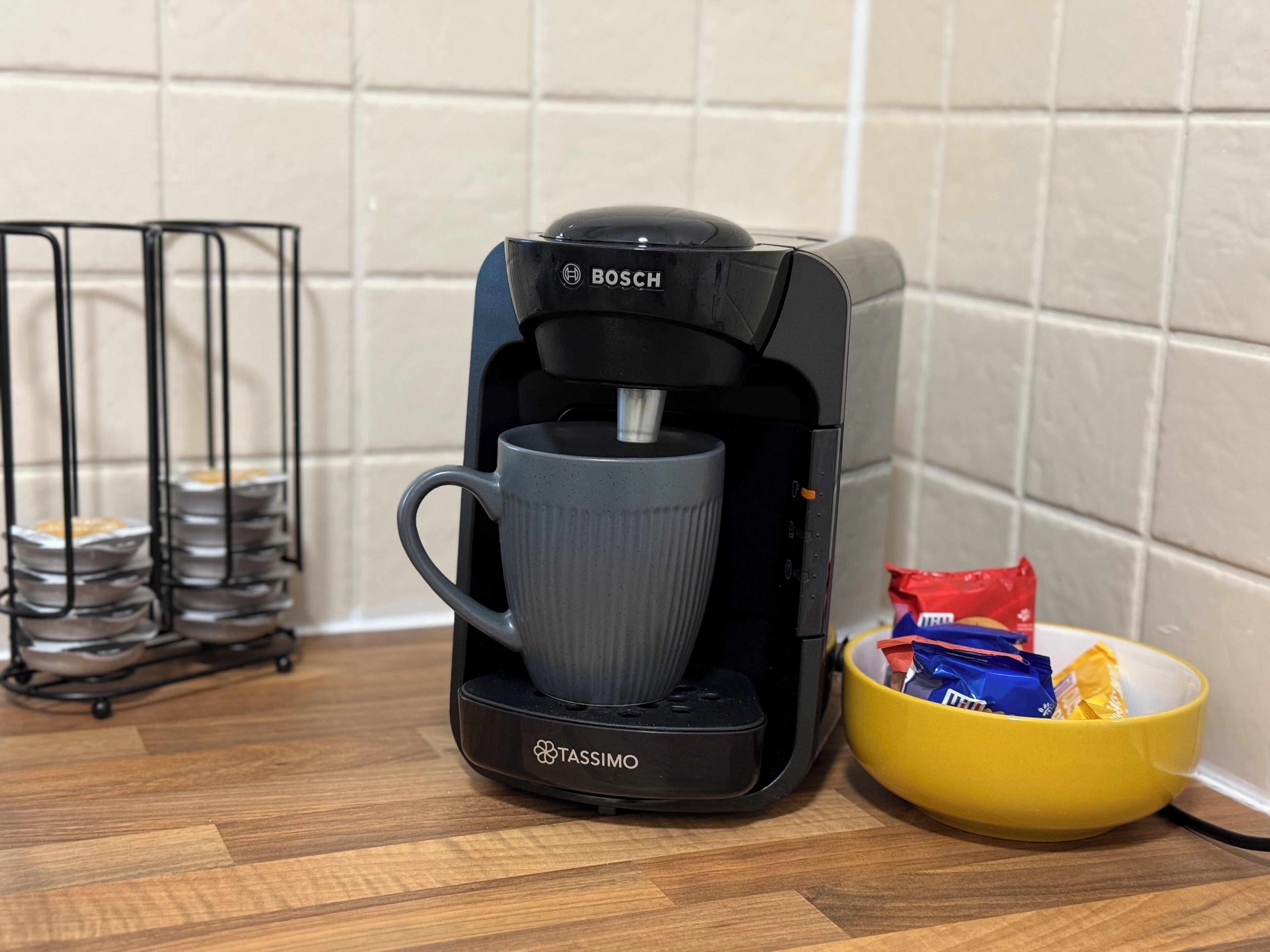 A coffee maker with a cup holder, a stack of plates, and a bowl of snacks on a wooden surface.