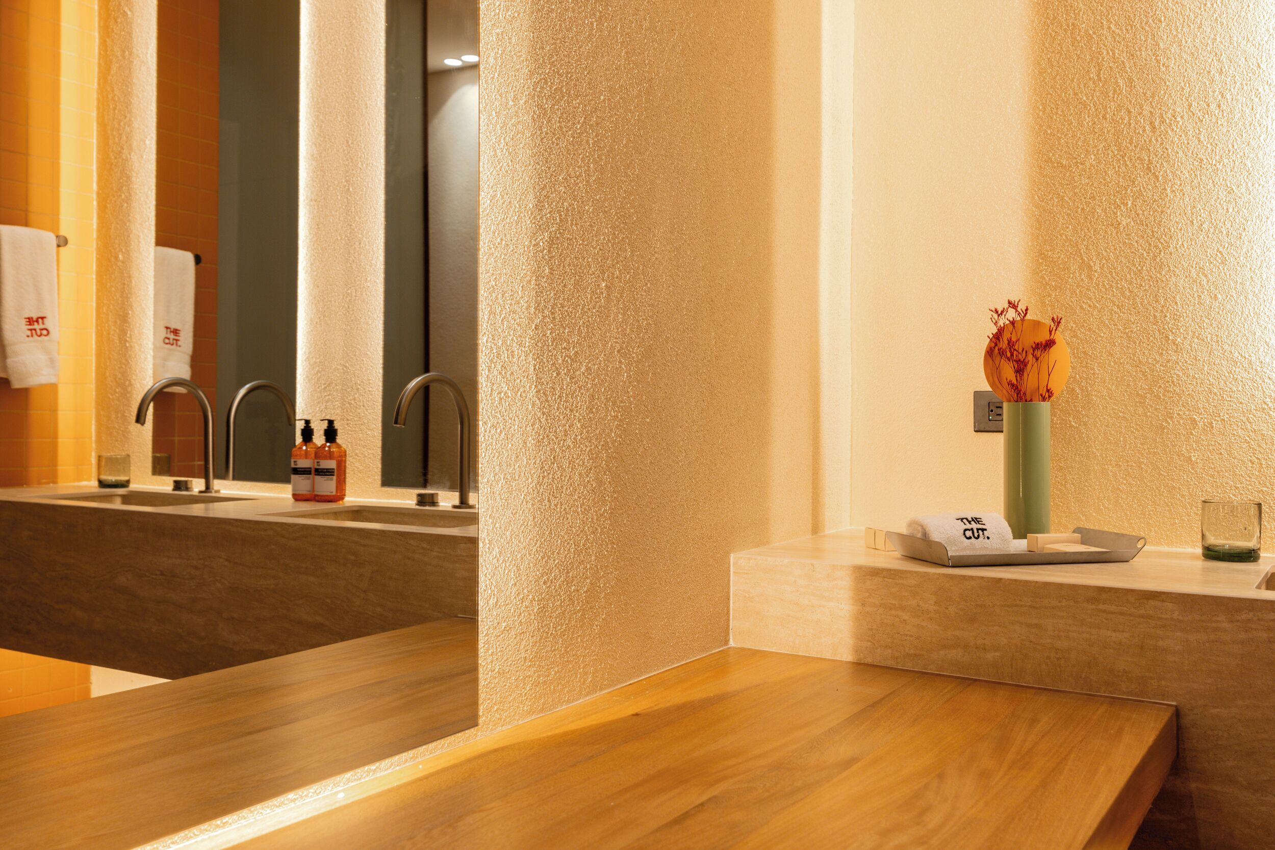A bathroom with a wooden vanity, a mirror, a towel rack, and a vase with dried flowers.