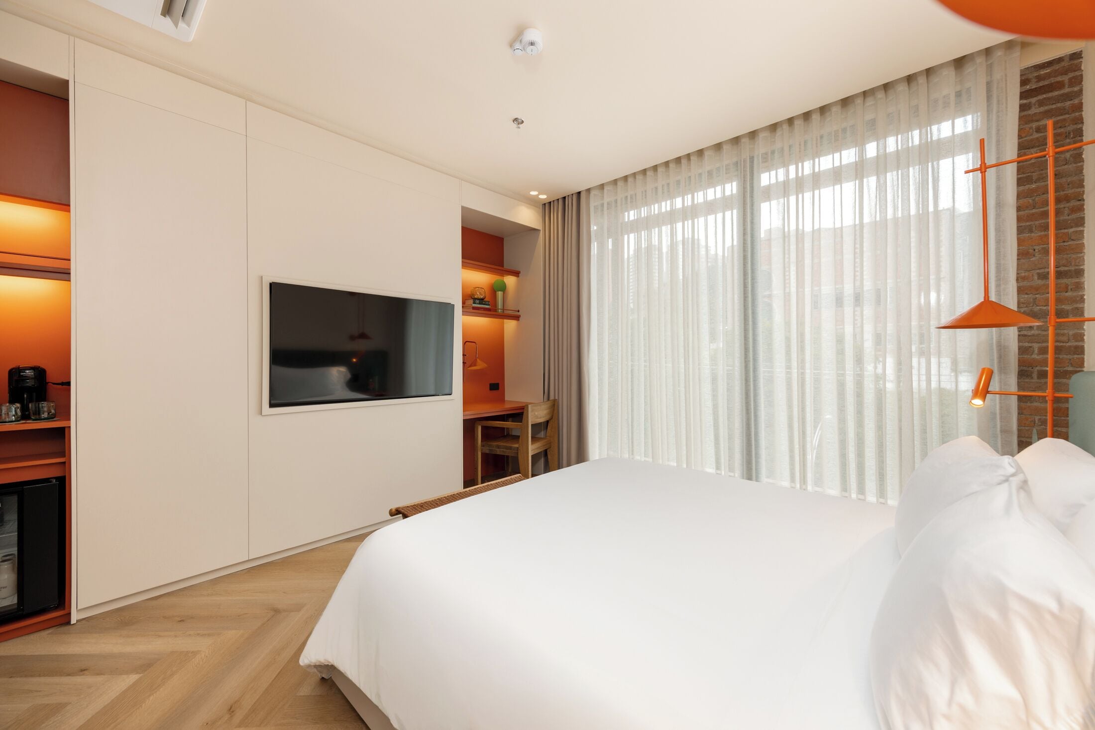 A hotel room with a bed, a TV, a desk, and a window with curtains.